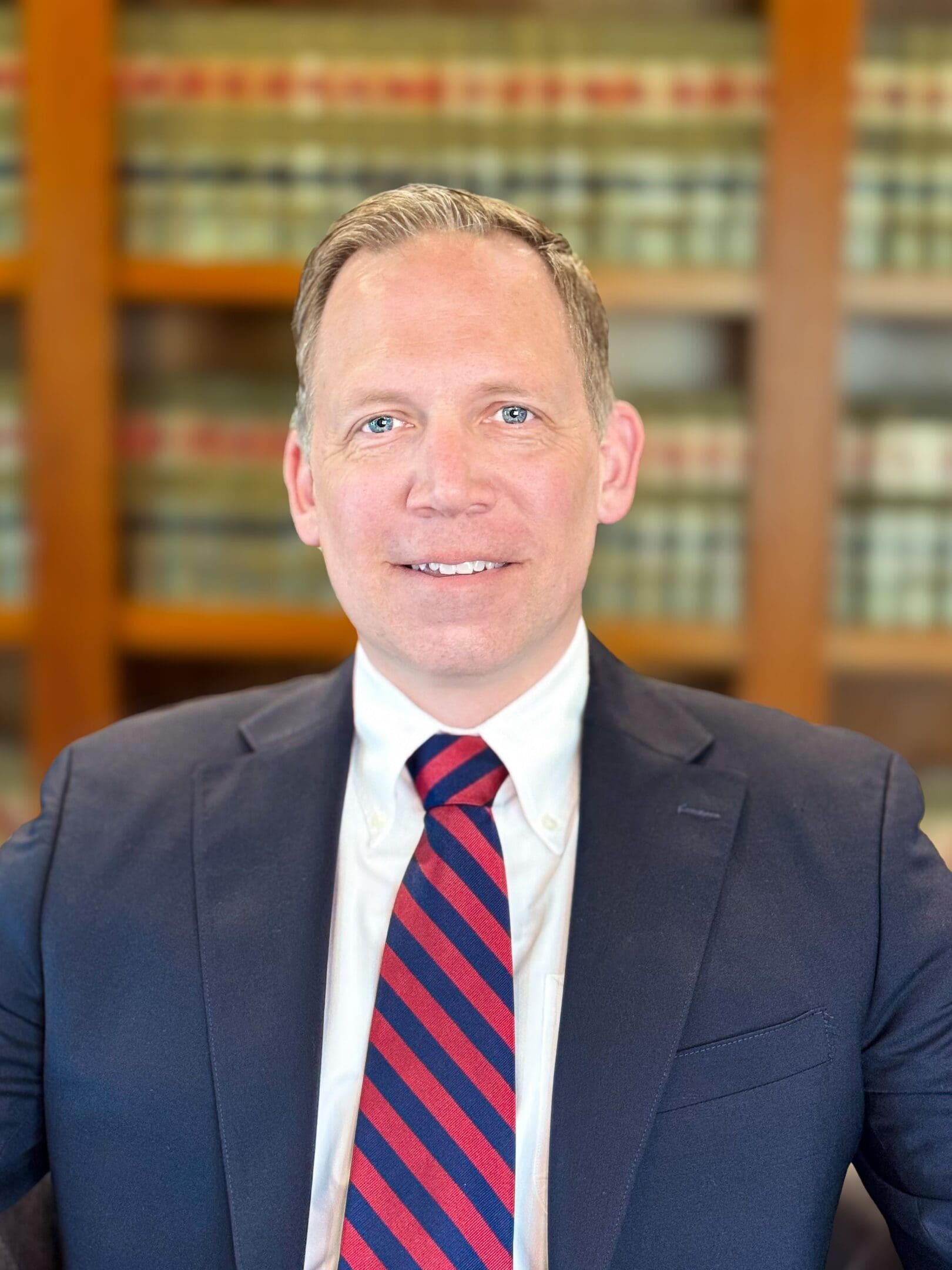 A man in suit and tie standing next to a book case.